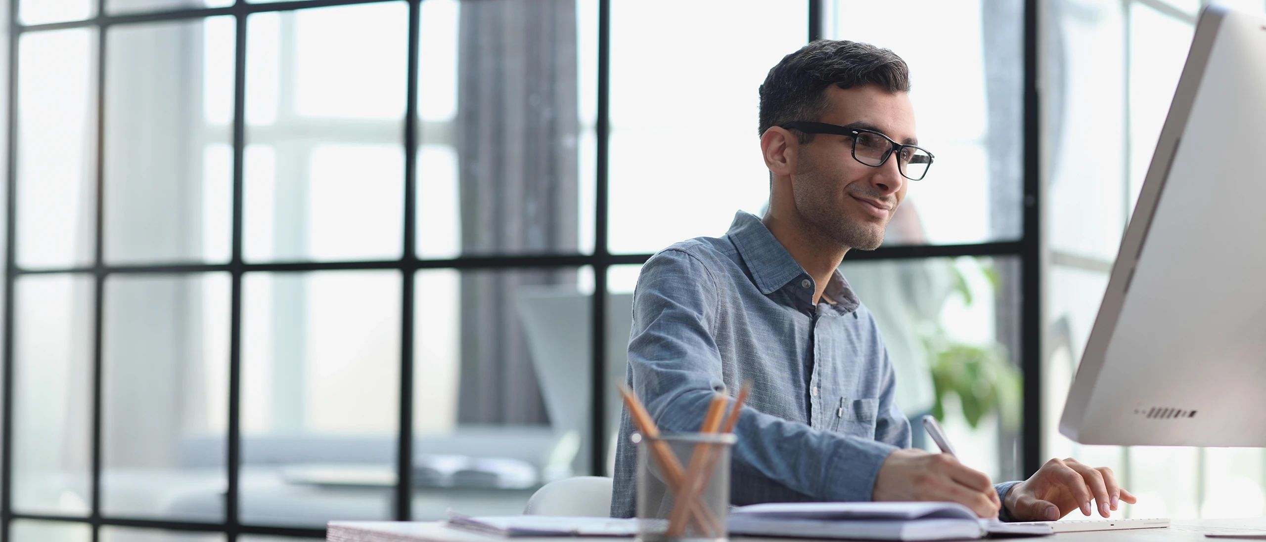 Mann arbeitet am Desktop-Computer und macht Notizen in einem modernen Büro
